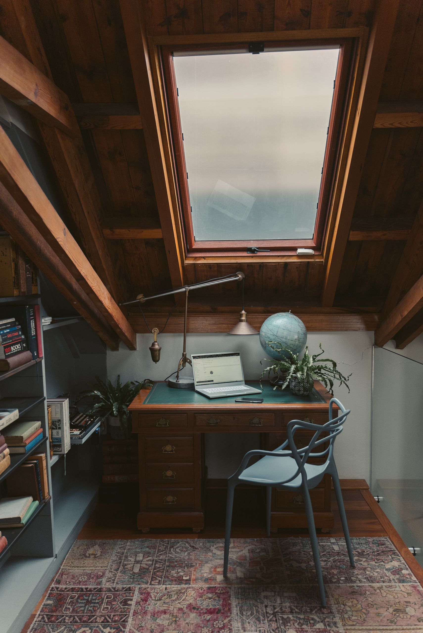 A tranquil home office setup in an attic with a skylight, desk, and laptop.
